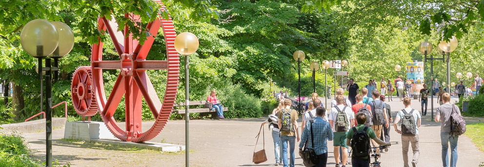 Students walking across Campus Nord. In The background there is a red sculpture of large gears.