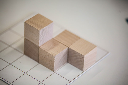 Kleine Holzwürfel liegen aneinander gereiht auf Papier mit Kästchen.